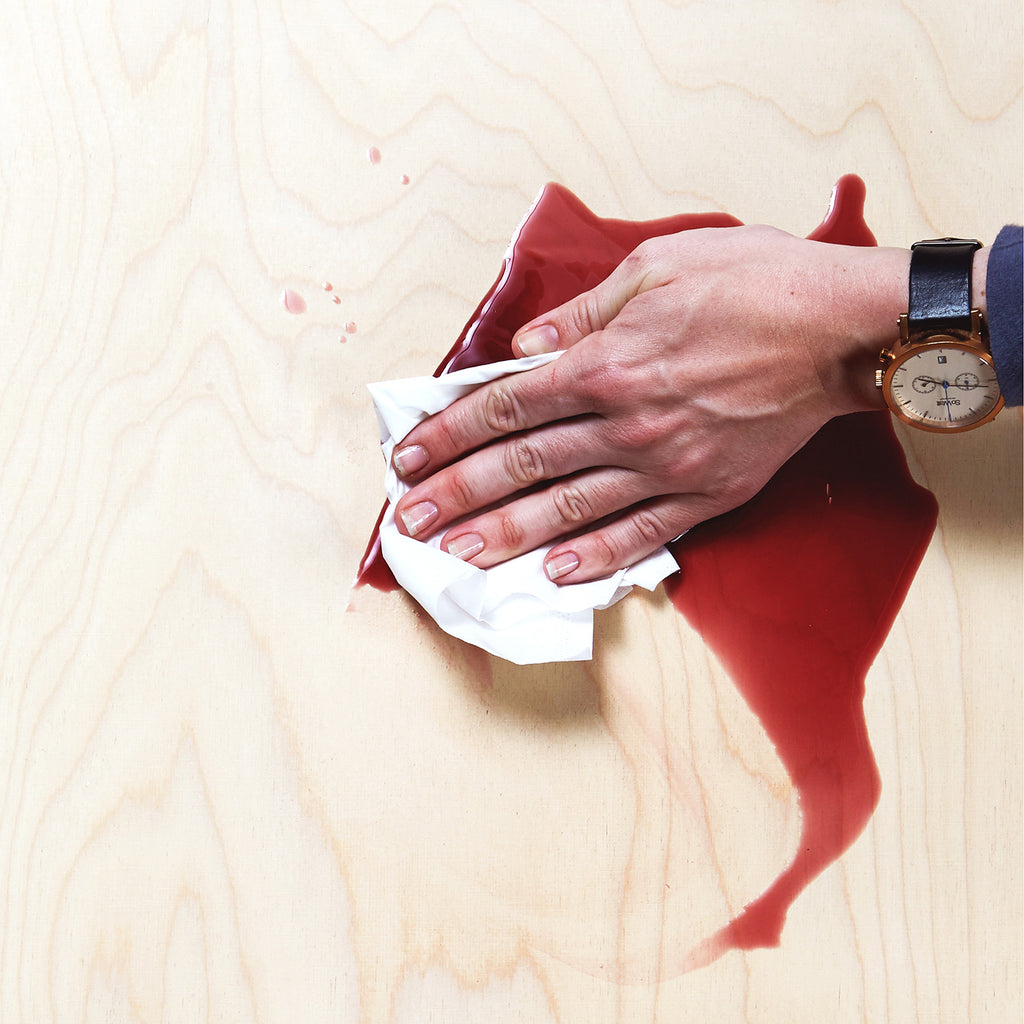 Hand with a Watch Wiping a Spilled Red Wine on a Wooden Surface