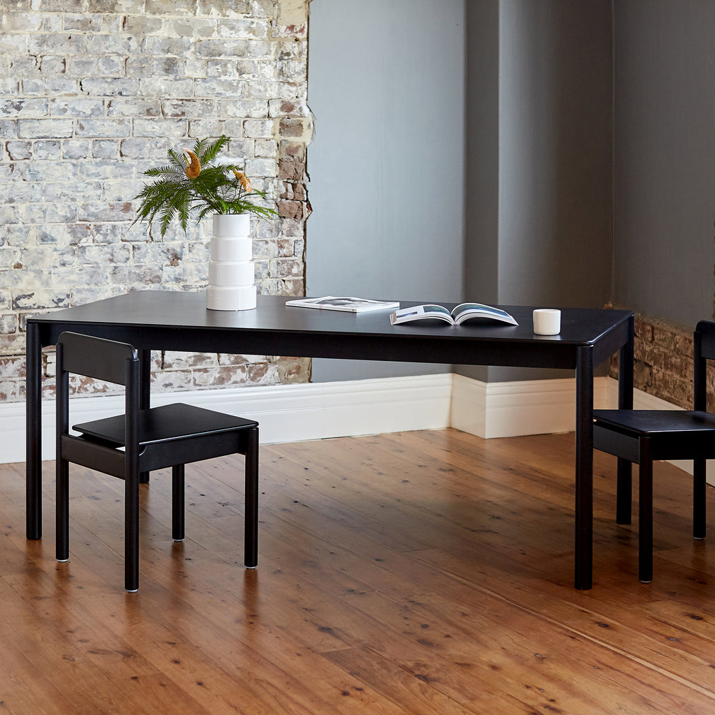 Minimalist Black Coloured Wooden Dining Table and Dining Chairs with Magazines and Floral Arrangement on Top