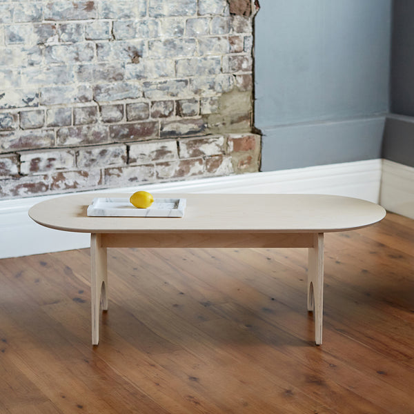 Natural Coloured Oval Shaped Plywood Coffee Table with Lemon on a Tray and Roughly Designed Brick Wall 